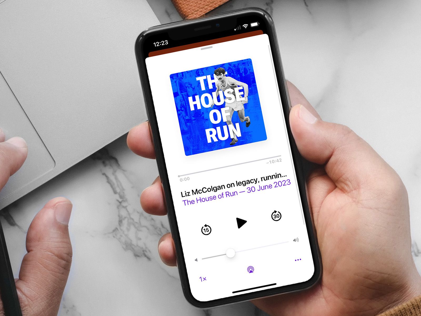 A hand holding a phone showing The House of Run podcast artwork and playback controls.