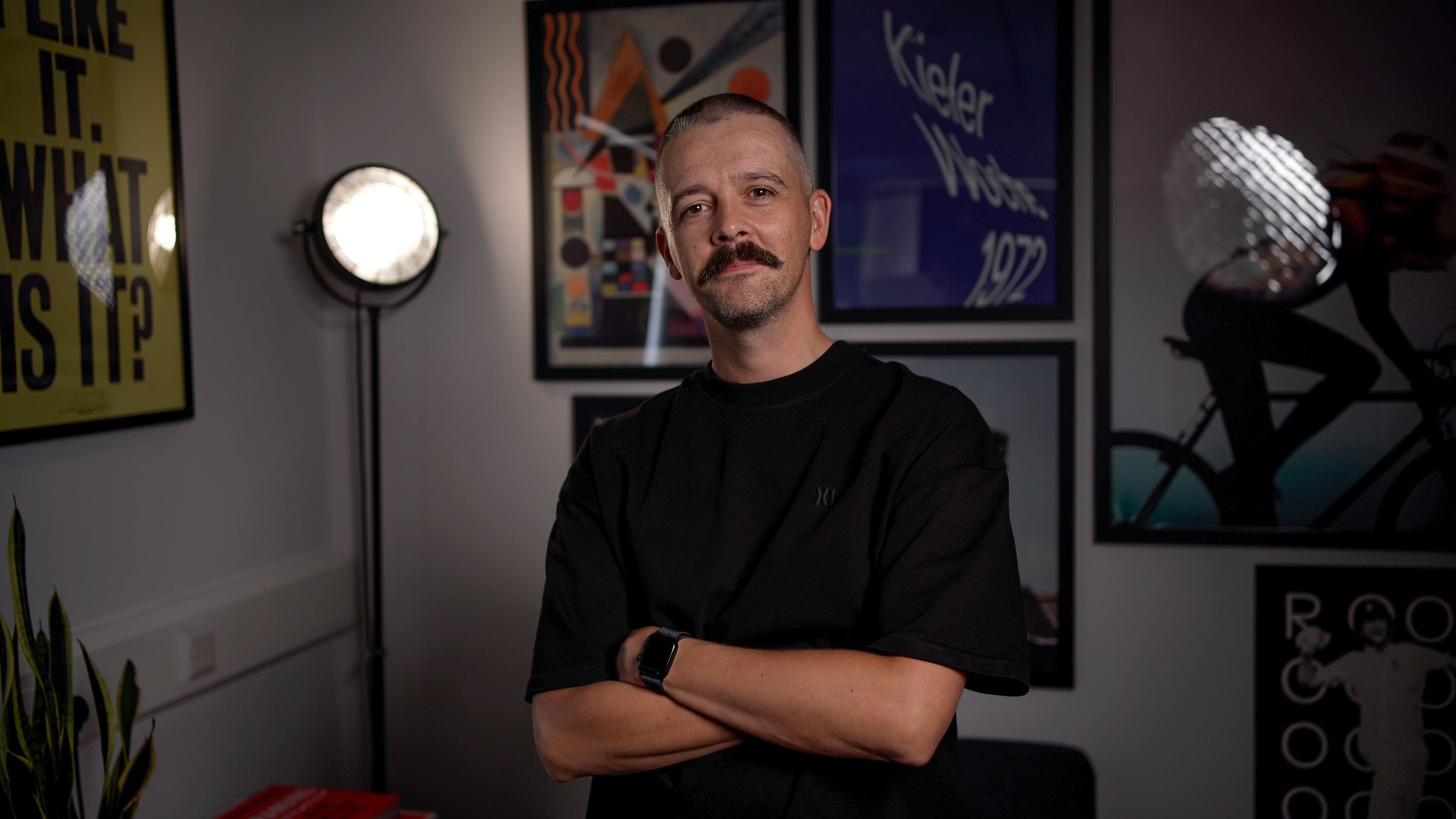 Matt Brunton standing with arms folded in front of framed artwork.