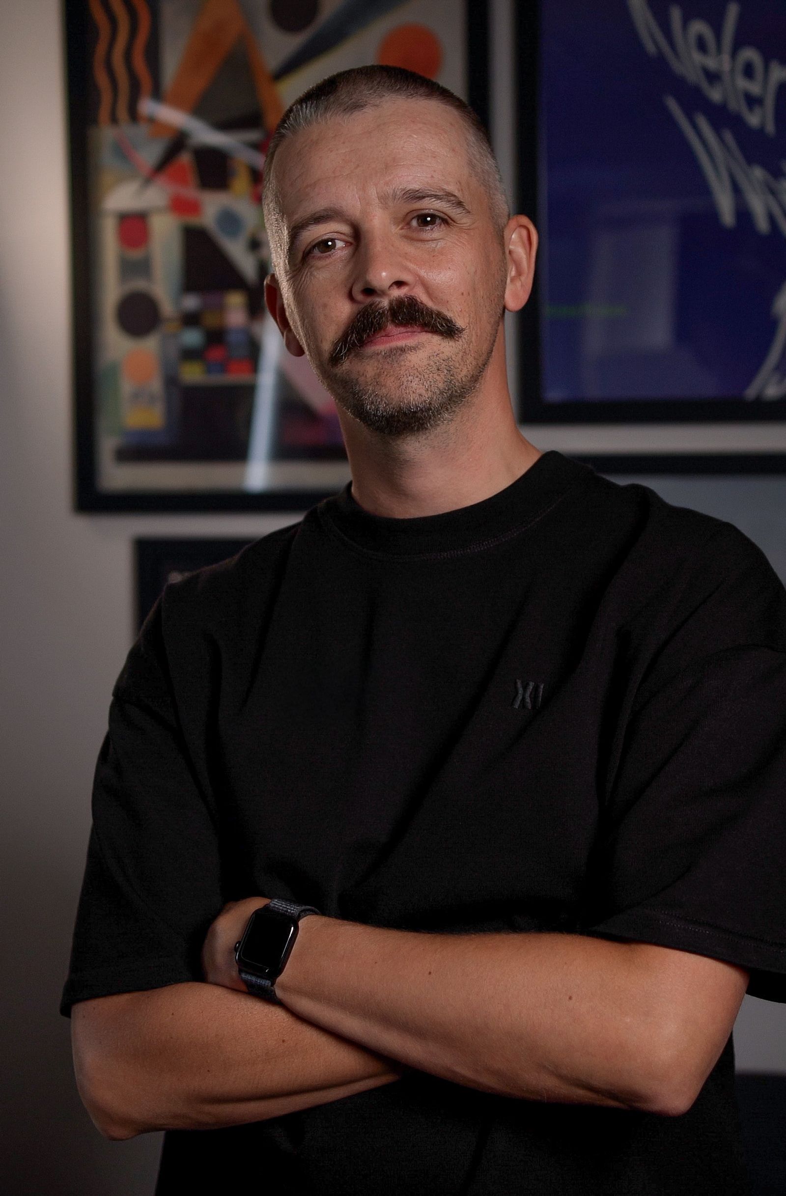 Matt Brunton standing with arms folded in front of framed artwork.