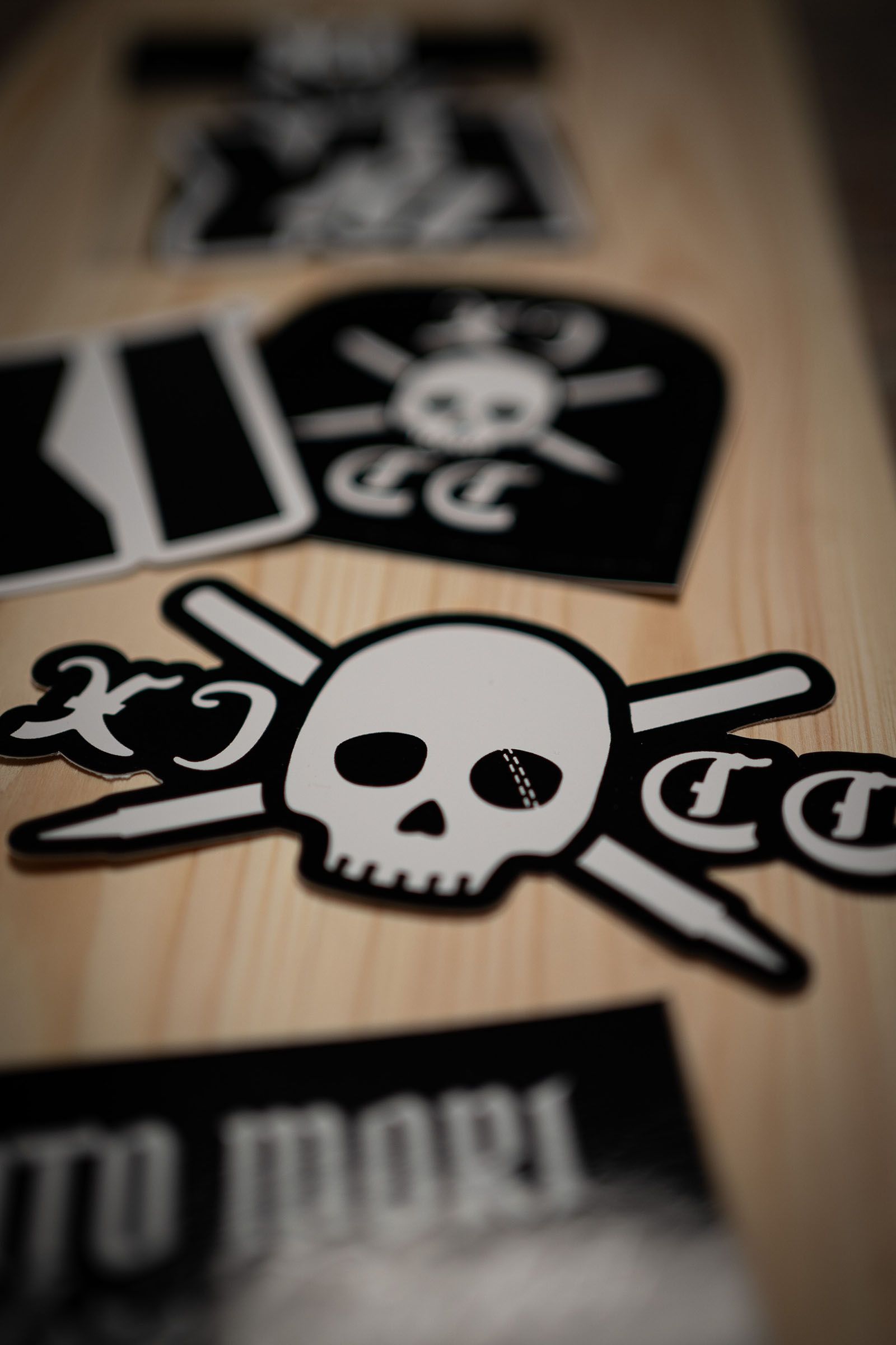 Close-up of black-and-white Eleven Cricket Club skull-and-crossed-bats stickers on pale wood.