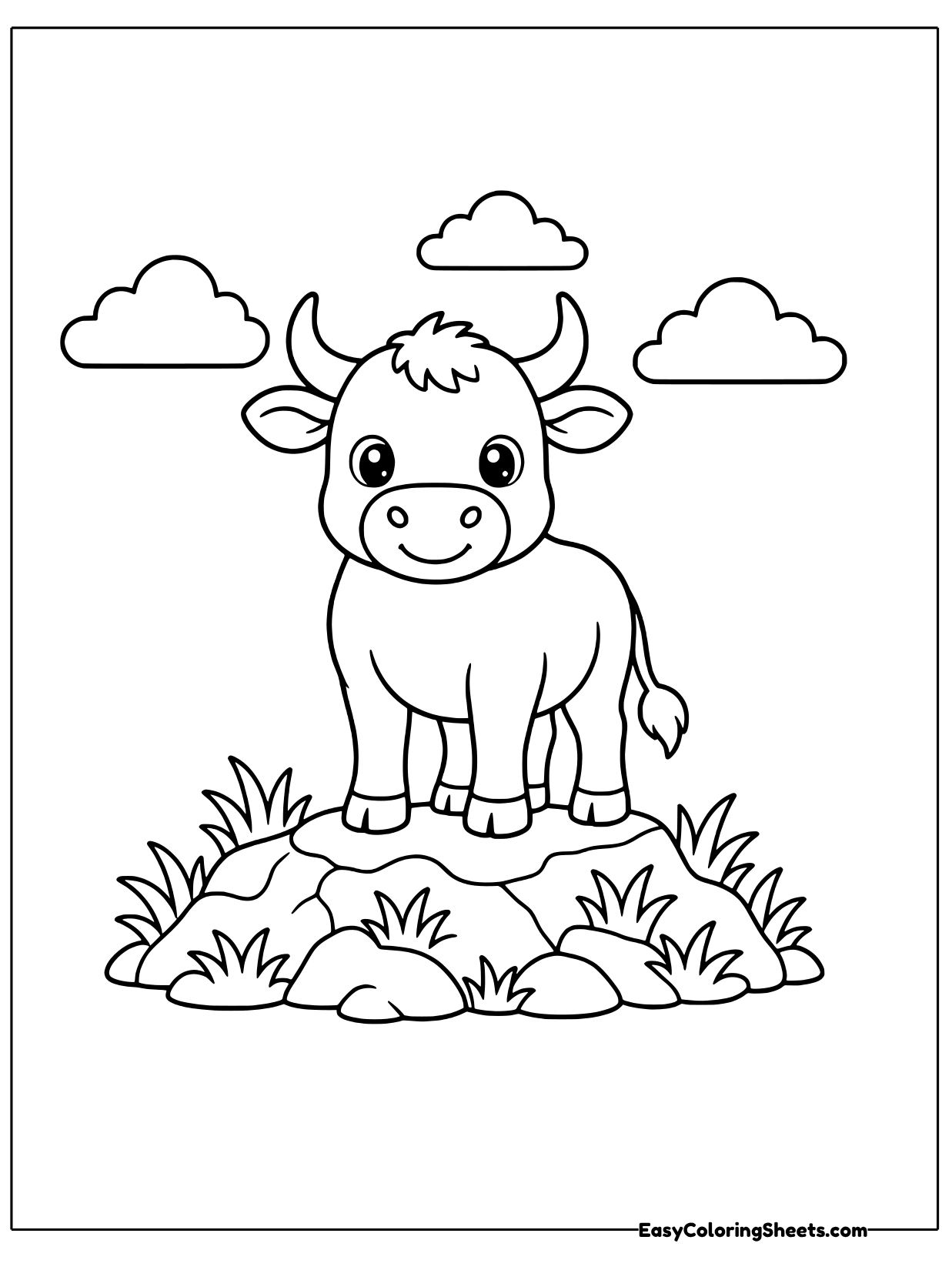 A cute bull with sturdy horns stands on a rocky ridge covered in grass, with clouds drifting around it.