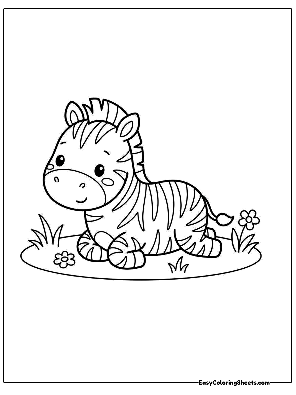 A baby zebra lies on a patch of grass with its legs tucked beneath it and tiny flowers growing nearby.