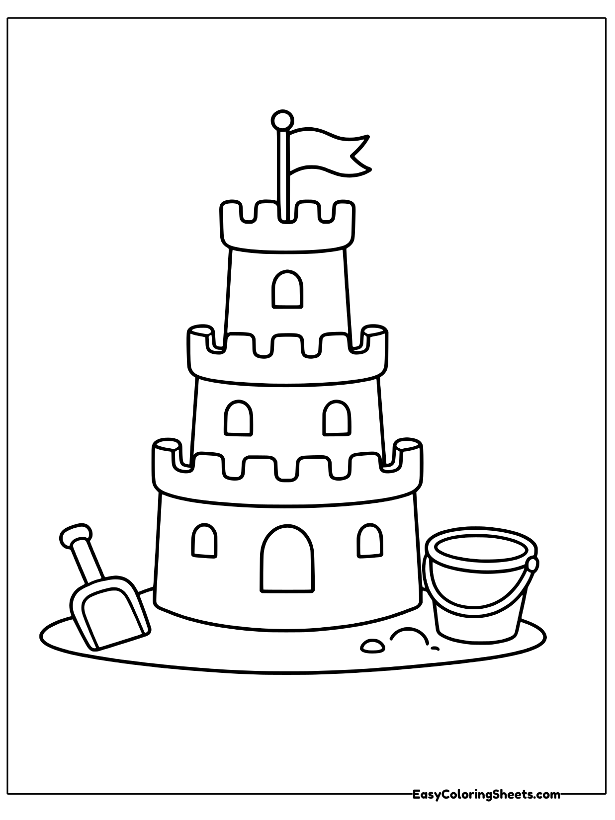A stacked sandcastle with round towers and a flag on top sits on the sand beside a shovel and a bucket.