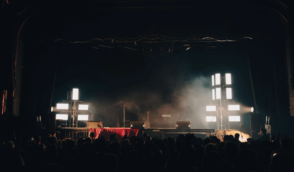 An empty stage with lighting towers on either side and a red drape across the floor of a riser which spreads across the stage.