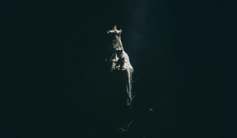 An all white statue of Mother Mary and Baby Jesus in stage lighting, on a dark background