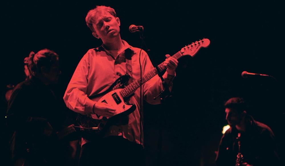 Artist King Krule on stage in red lighting, holding a guitar