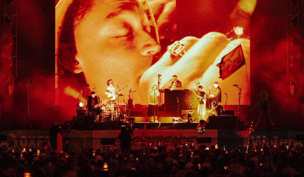 Loyle Carner on the Glastonbury stage with a photo of him in a close up camera angle on the upstage screen.