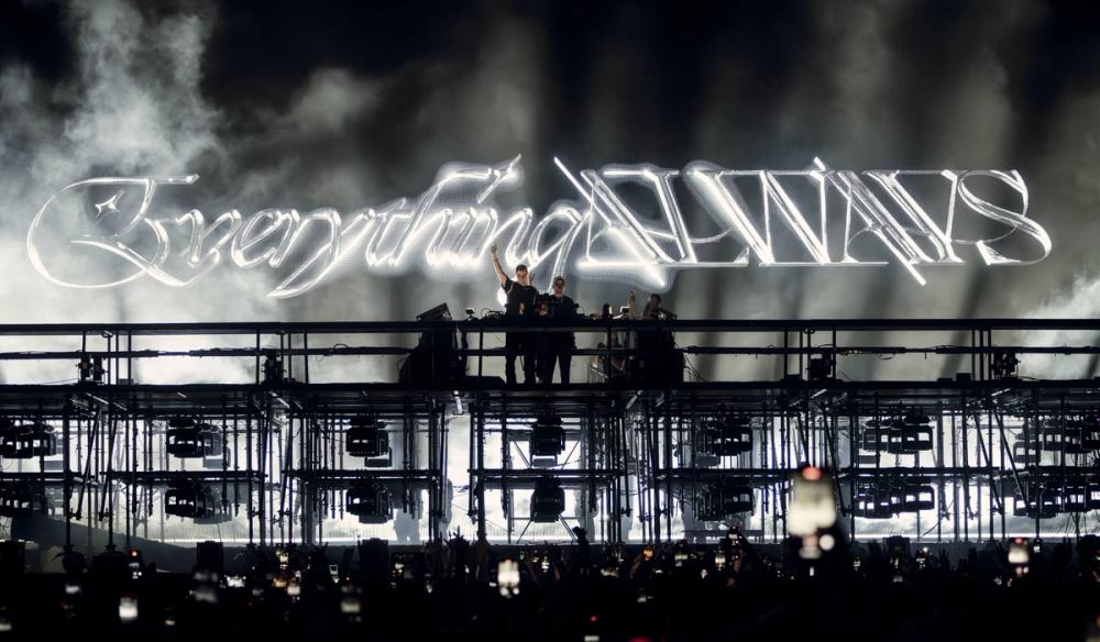 John Summit and Dom Dolla stand on stage in front of a glowing "Everything Always" logo