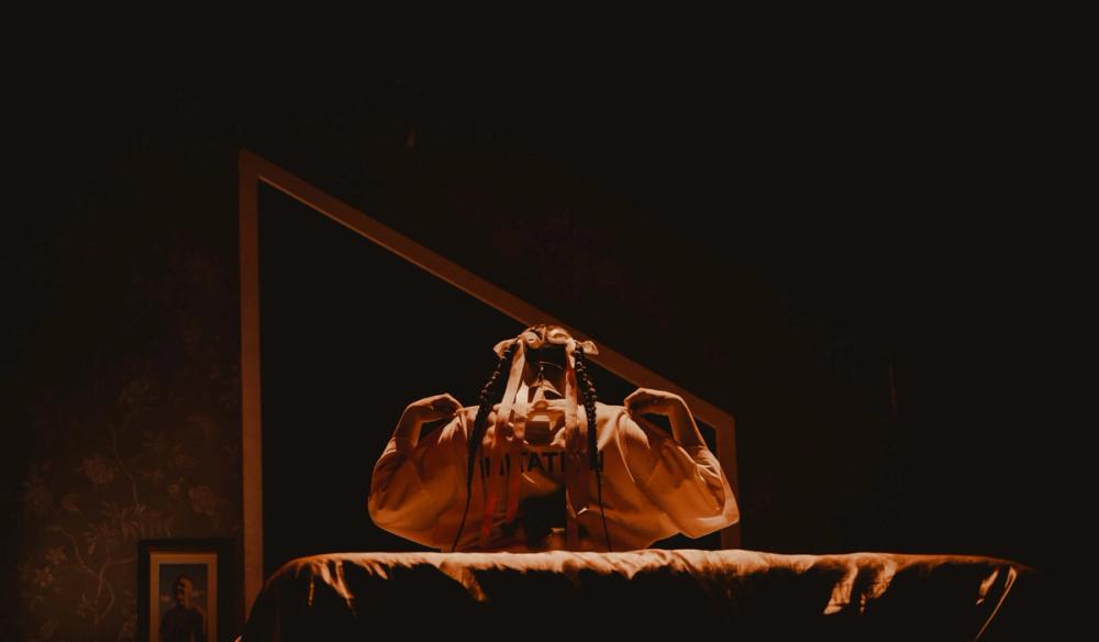 Anne-Marie sits with her back to the camera adjusting her shirt in a mirror in front of her.