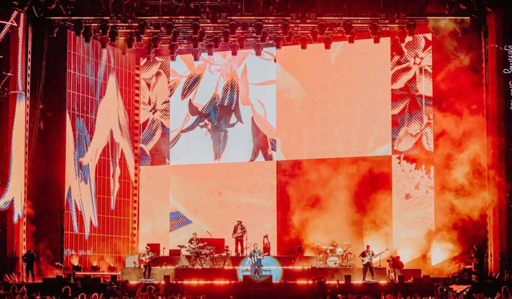 A close up of a stage with gridded screen content in reds and oranges behind Sam Fender and his band.