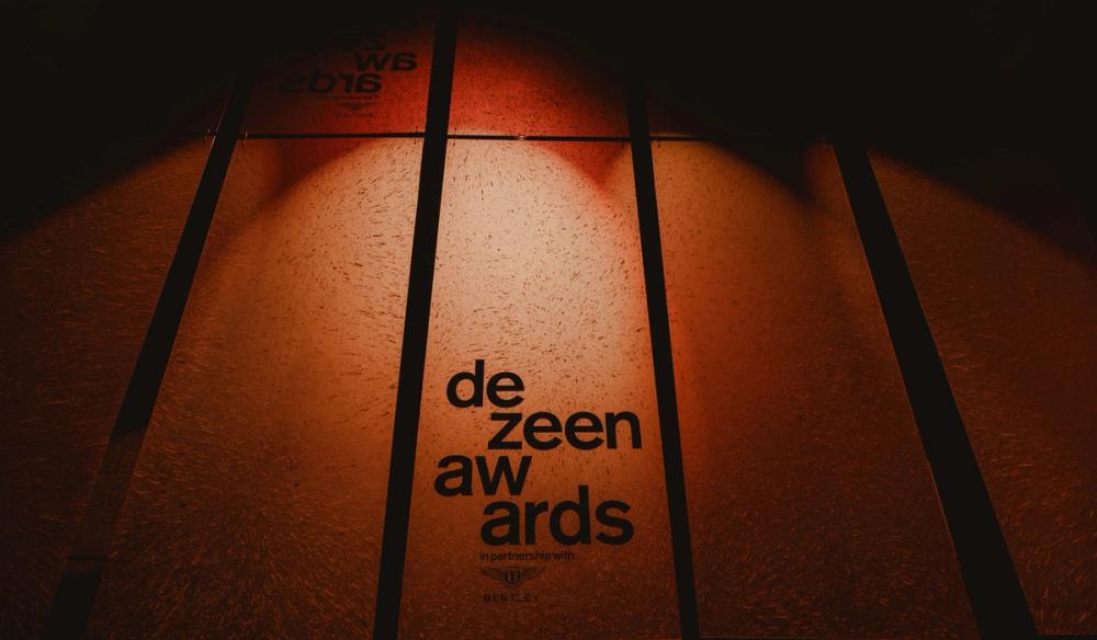 Five rows of hanging, orange lit, Smiles Plastic sheets with the Dezeen Awards logo etched into the central row. 