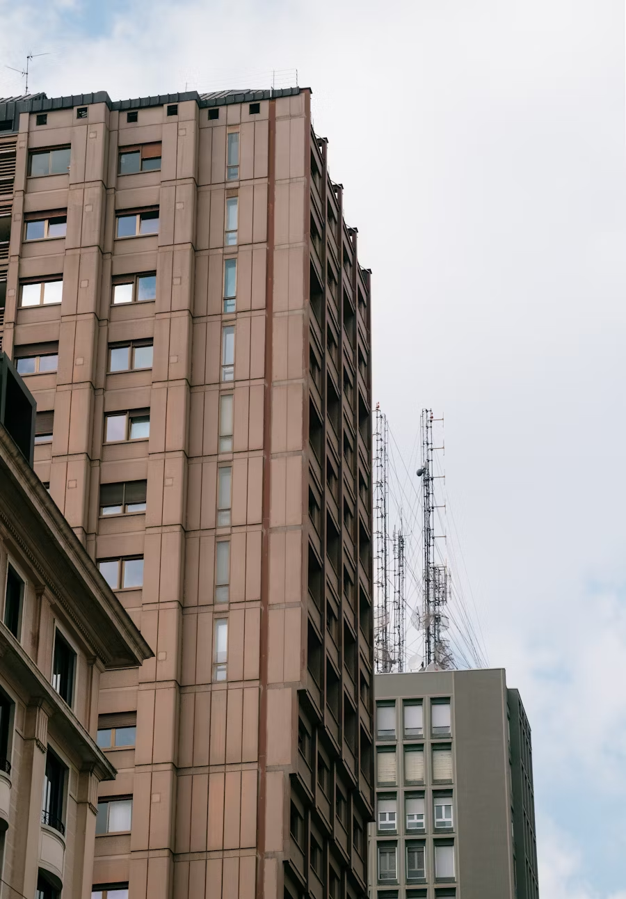 Looking up at the upper floors of tall apartment buildings against a pale sky.