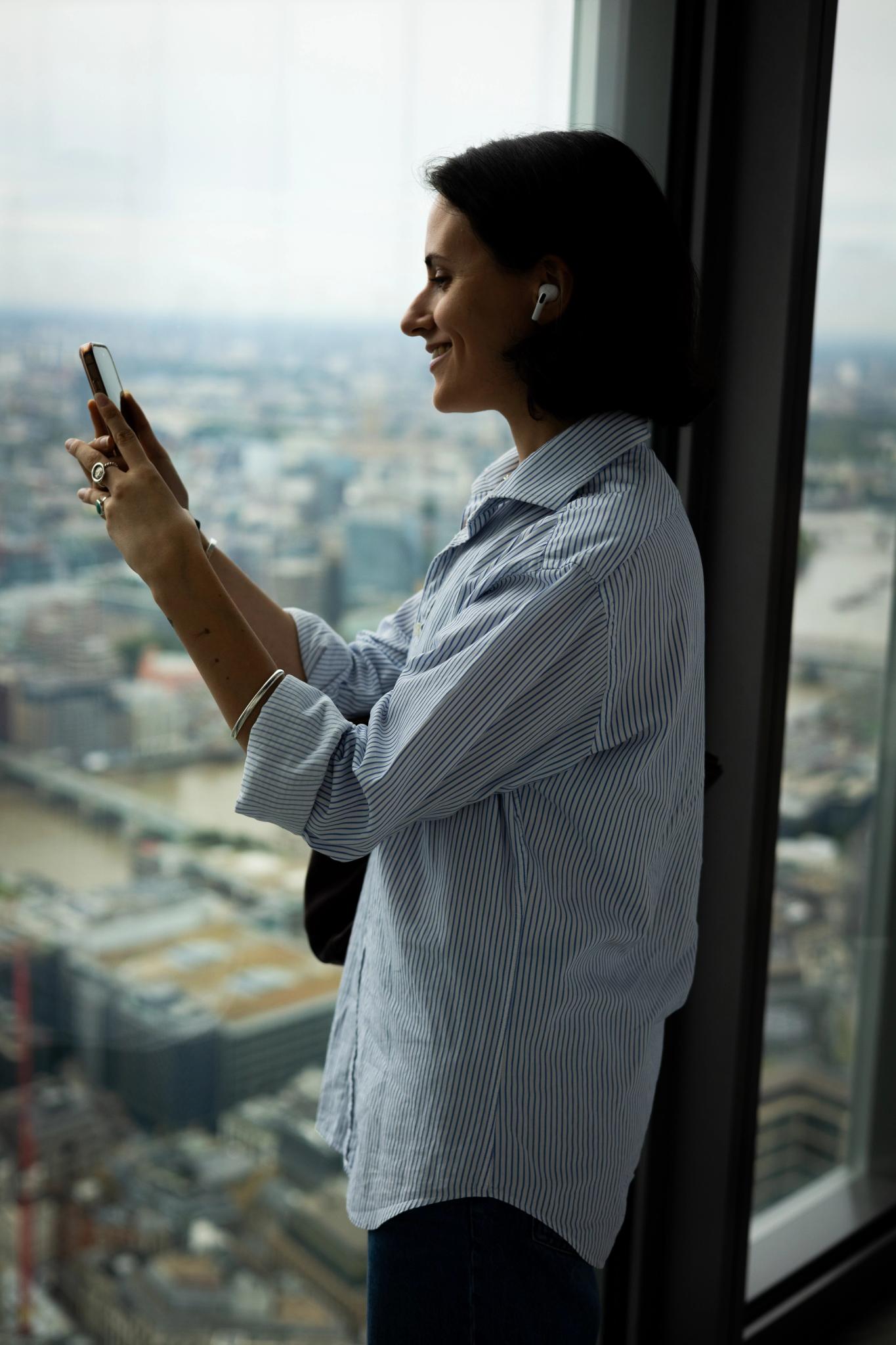 Woman looking at her phone next to window with view over a city