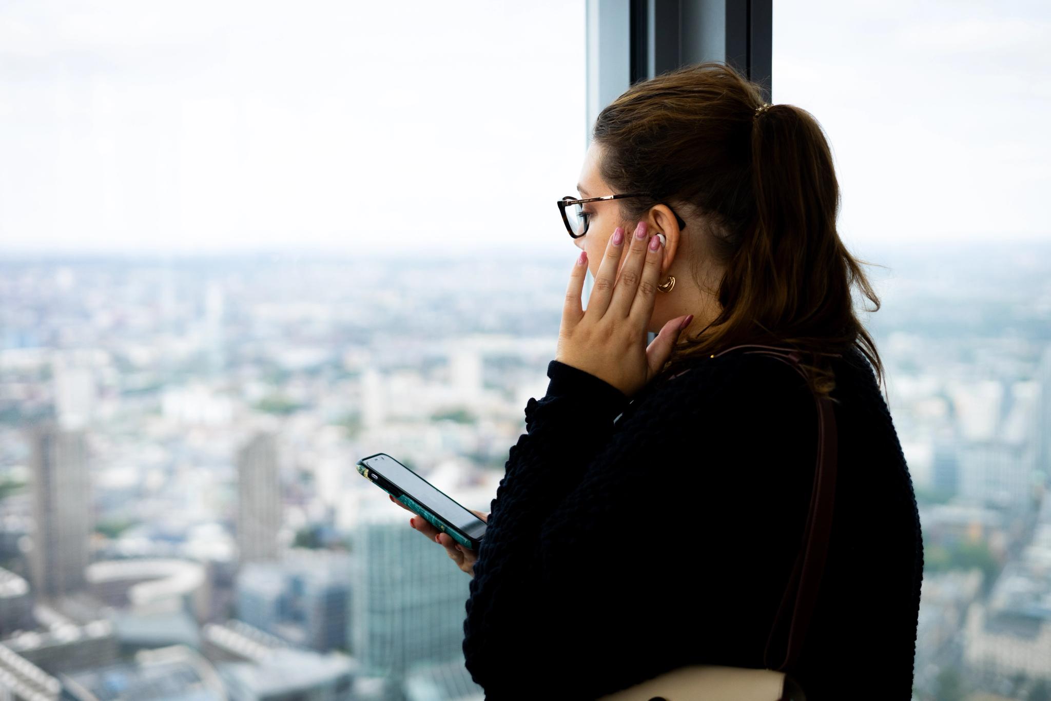 Lady listening to the audio guide via her mobile phone overlooking the city of London