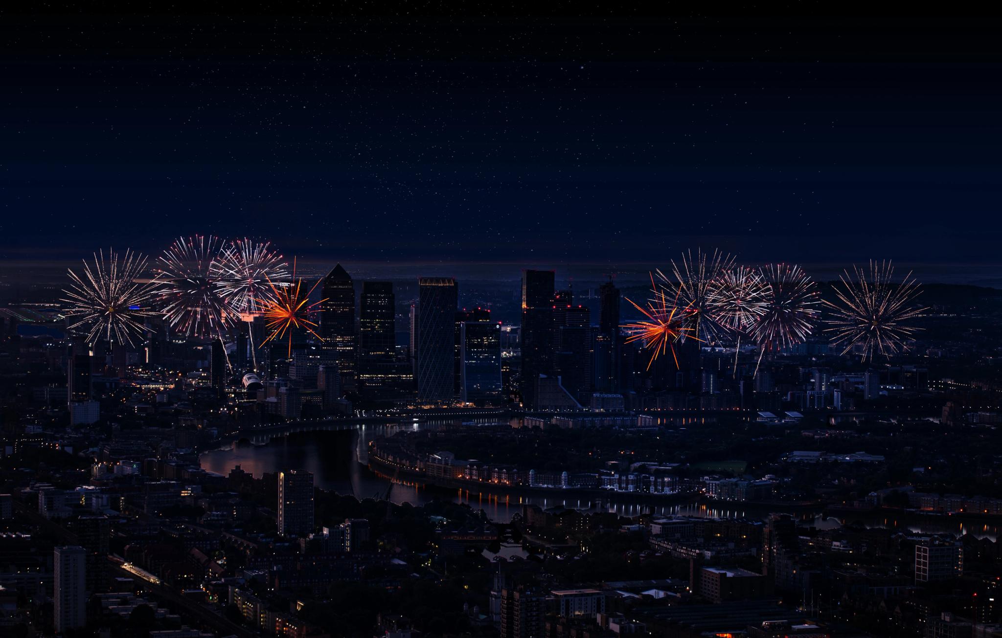 A floral arrangement featuring sculpted white flowers and delicate pink and yellow blossoms displayed on soft pink fabric, with city buildings and a sunset sky visible through large windows in the background.