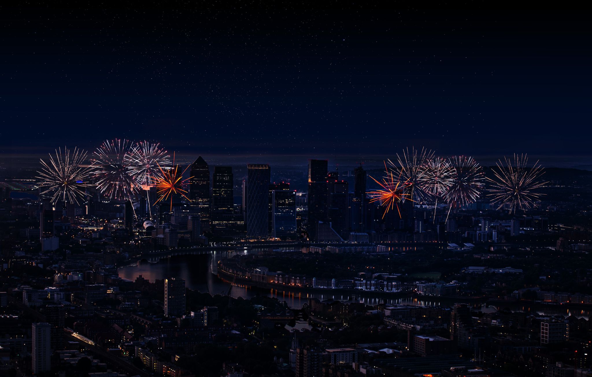 A floral arrangement featuring sculpted white flowers and delicate pink and yellow blossoms displayed on soft pink fabric, with city buildings and a sunset sky visible through large windows in the background.