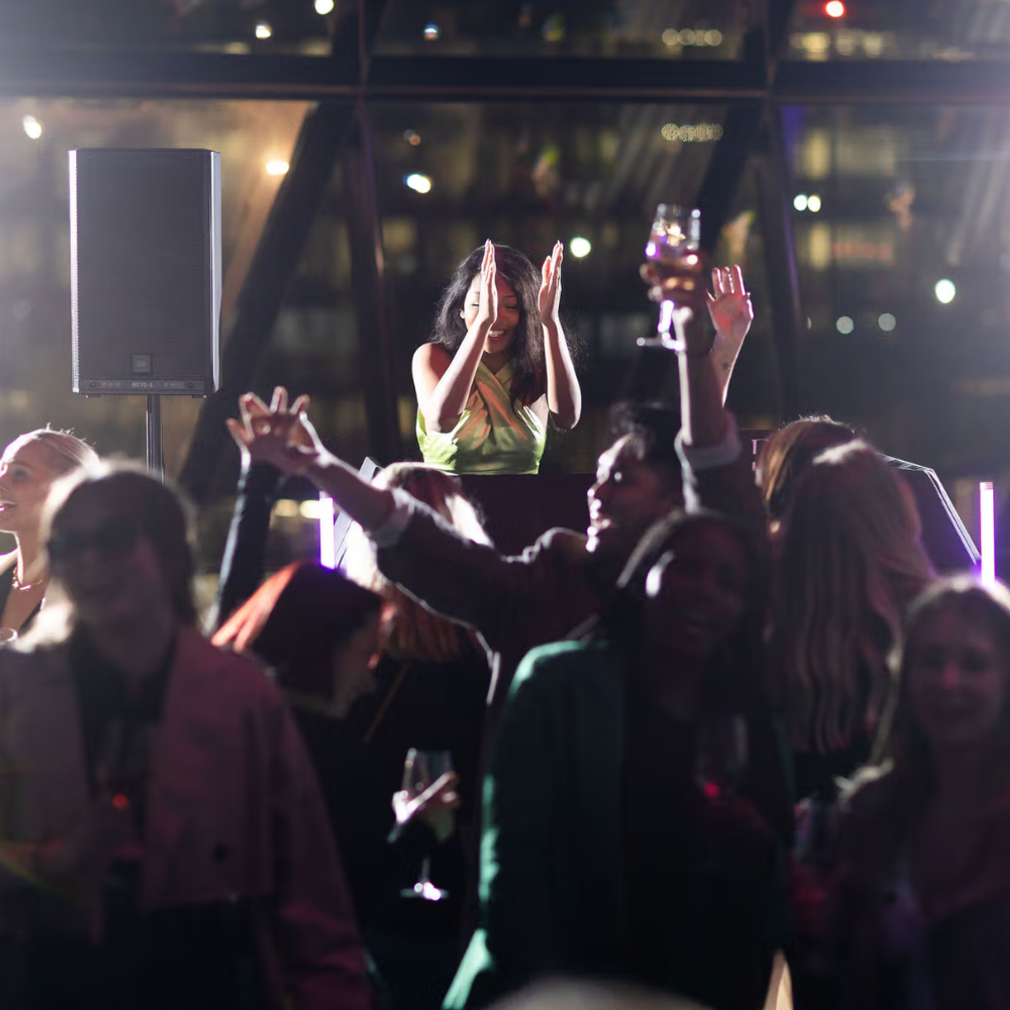 DJ performing for a lively crowd at a party, with people dancing, raising glasses, and enjoying the vibrant celebration under bright lights. 