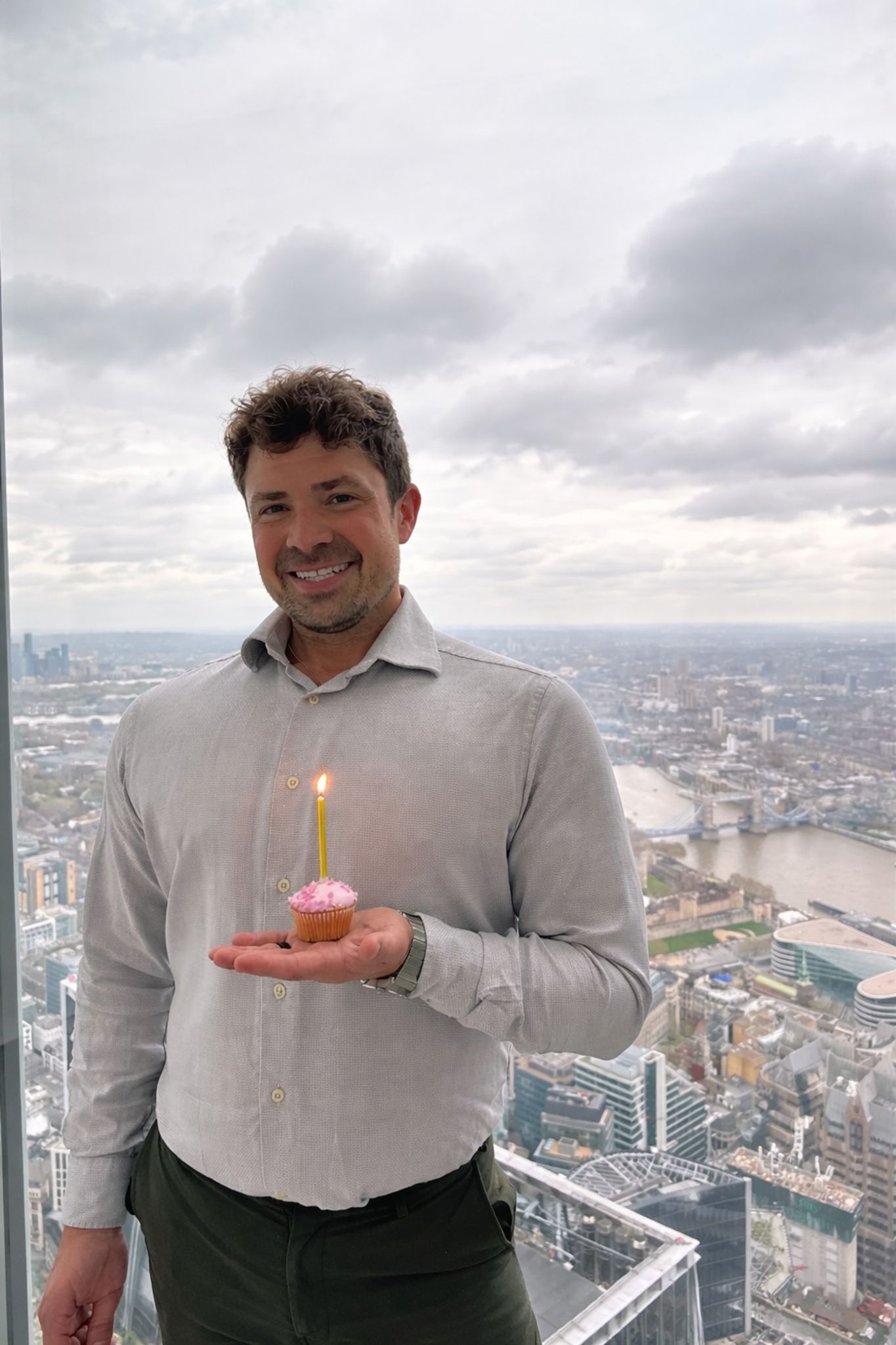 A man holding a cupcake with a candle overlooking London