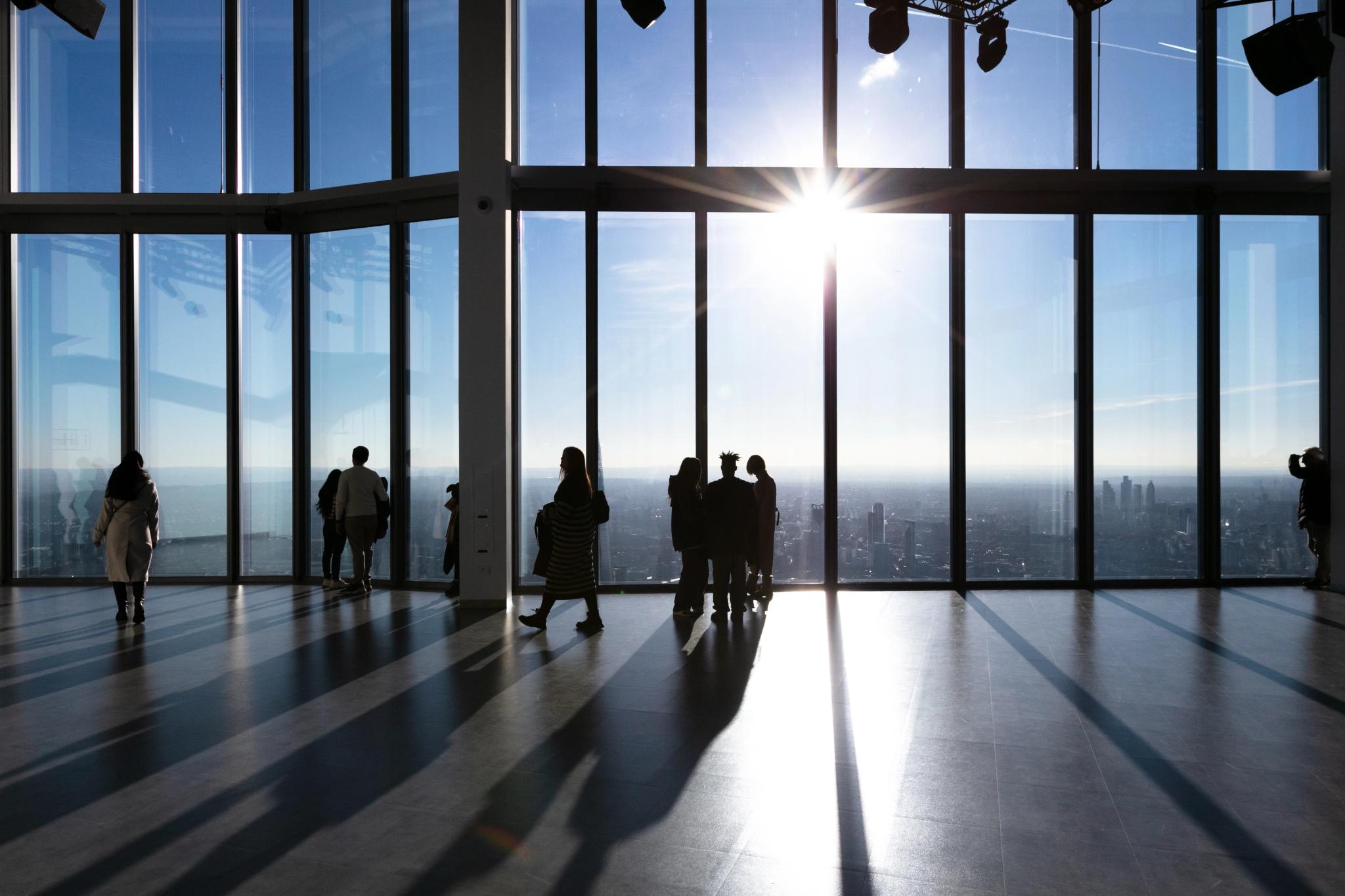 People standing next to large glass windows with a view of the London skyline