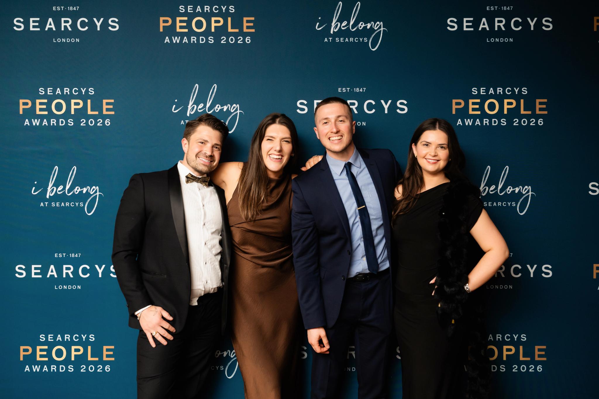 A group of people in formal wear stood in front of a Searcy's People Awards 2006 hoarding