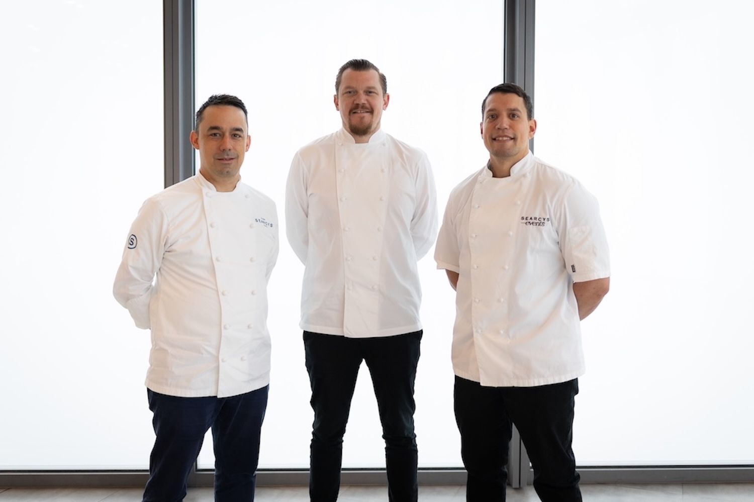The chef Alex Dilling stood between two other men posing for a photo. All three men are wearing chef's whites.