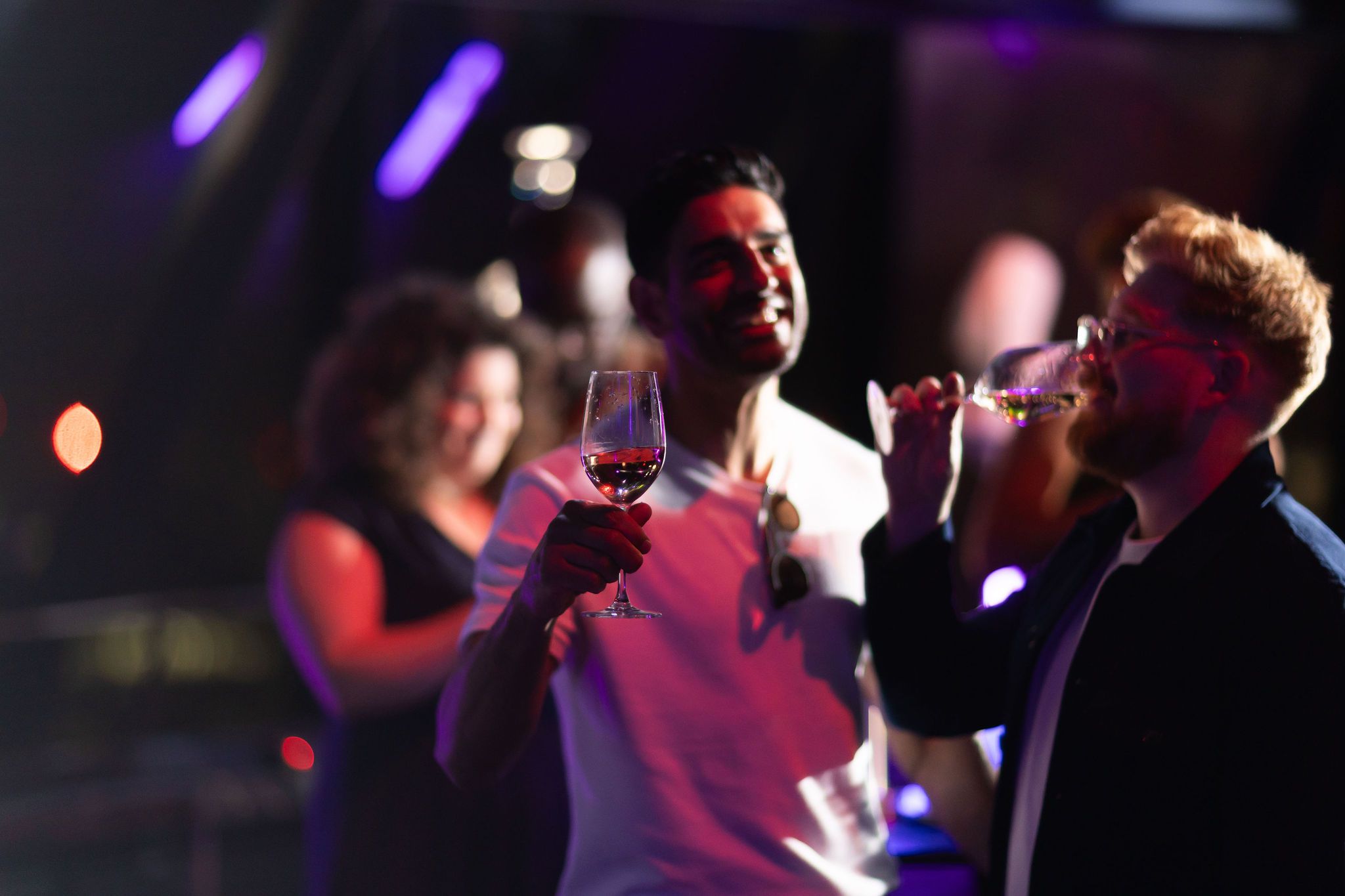 A floral arrangement featuring sculpted white flowers and delicate pink and yellow blossoms displayed on soft pink fabric, with city buildings and a sunset sky visible through large windows in the background.