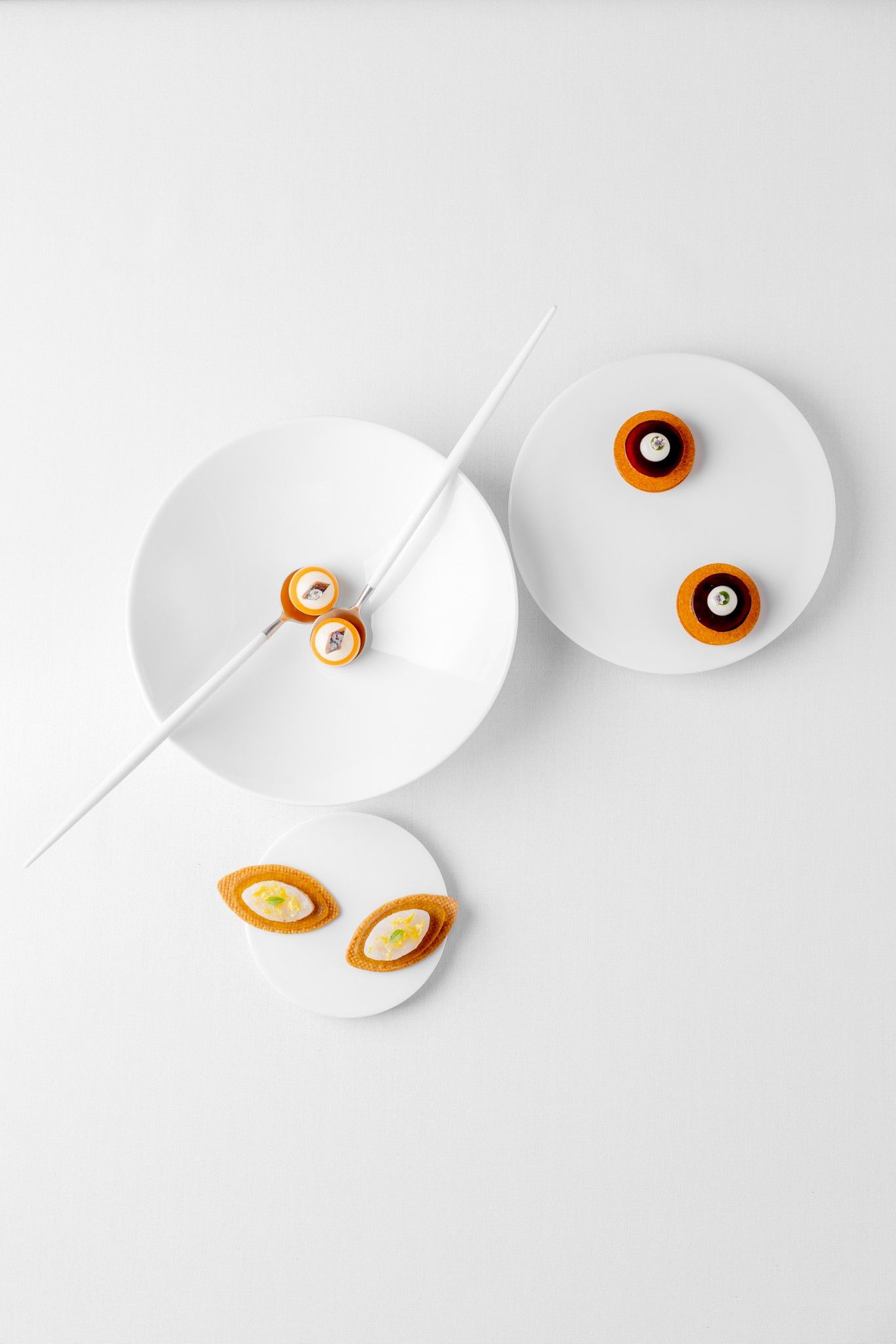Minimalist fine dining dish with small tartlets and canapés arranged on white plates.