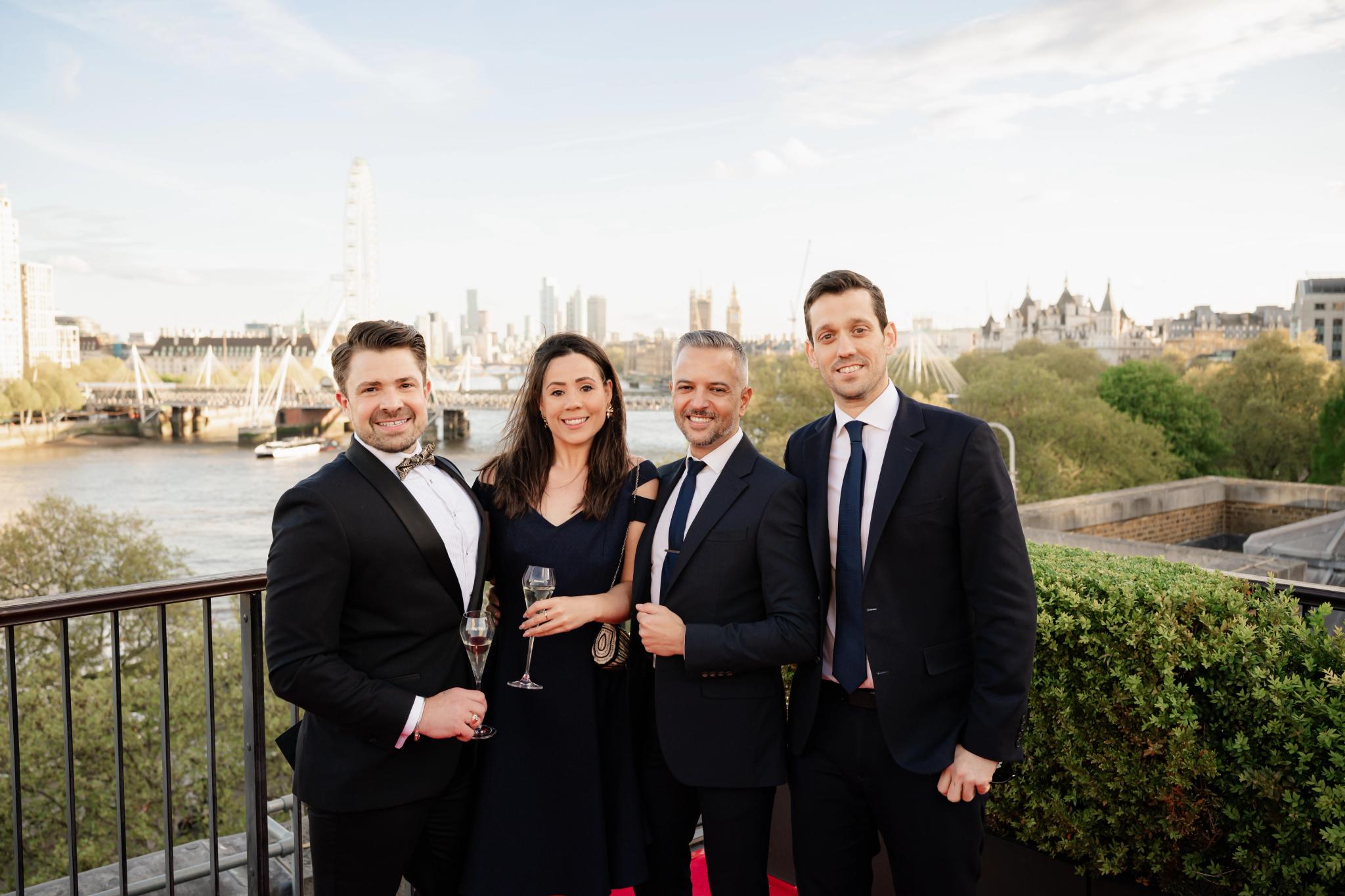 A group of people in formal attire on a balcony overlooking the River Thames