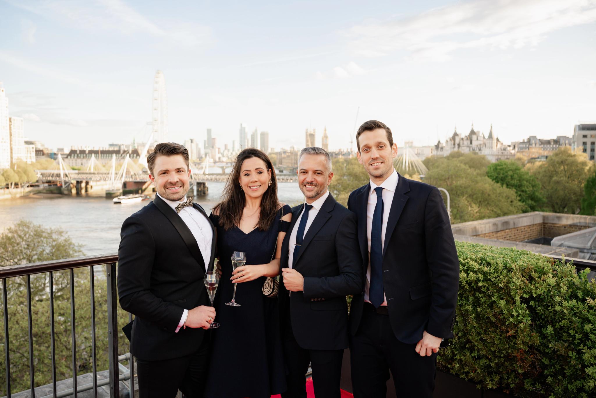 A group of people in formal attire on a balcony overlooking the River Thames