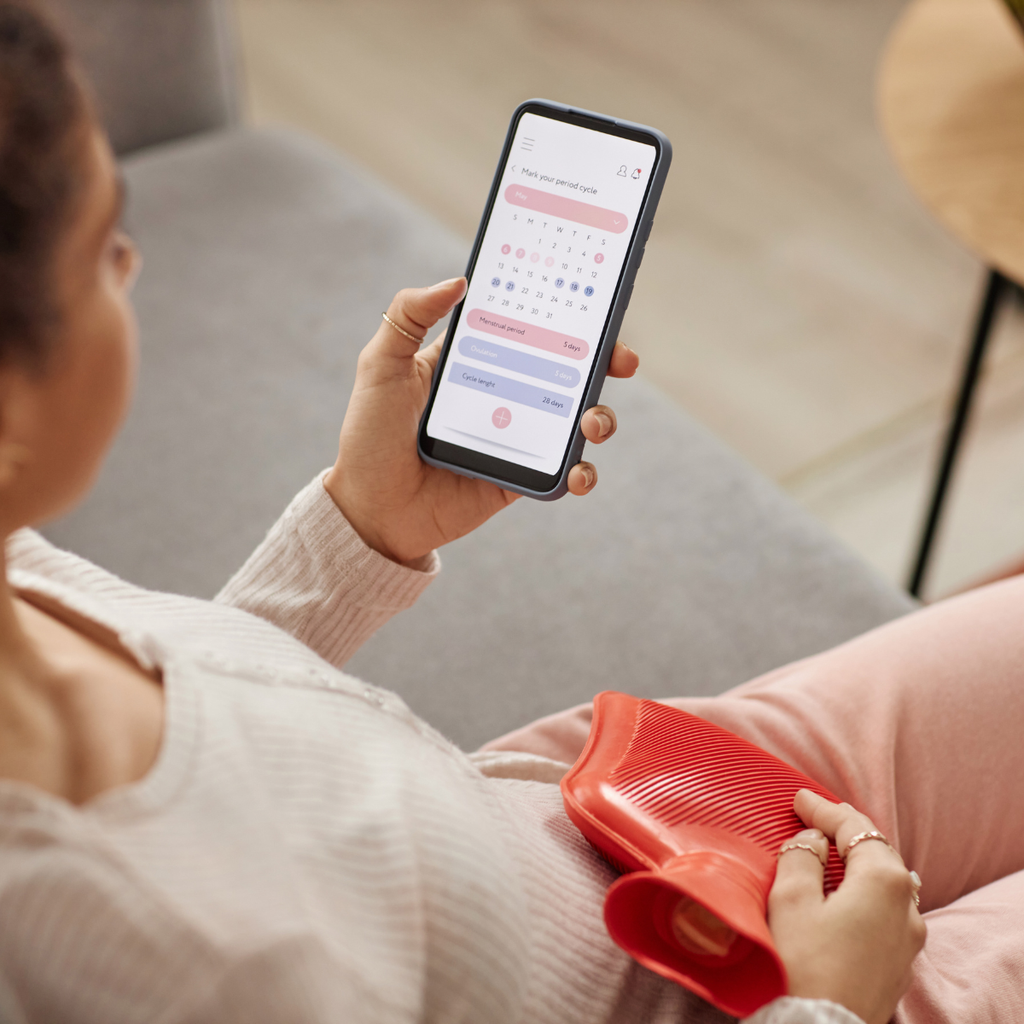 Person mit Wärmeflasche und Zykluskalender in der Hand