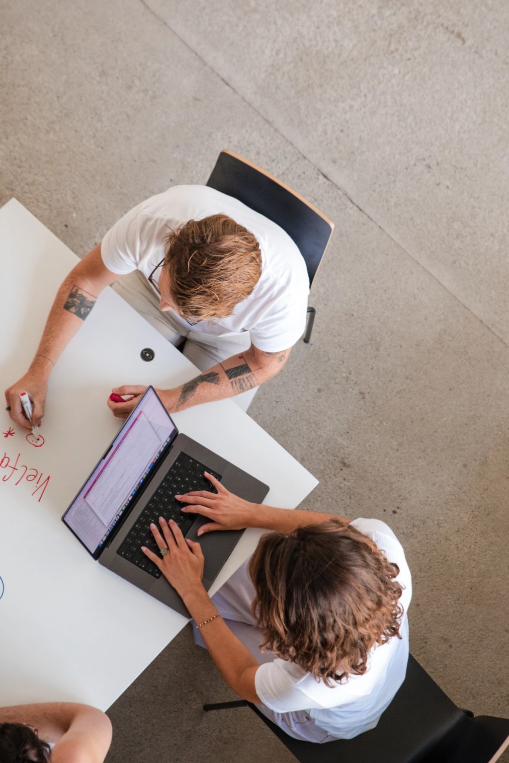 2 Menschen arbeiten mit anderen rund um einen Tisch mit einem Laptop. Ansicht von oben auf ihre Köpfe