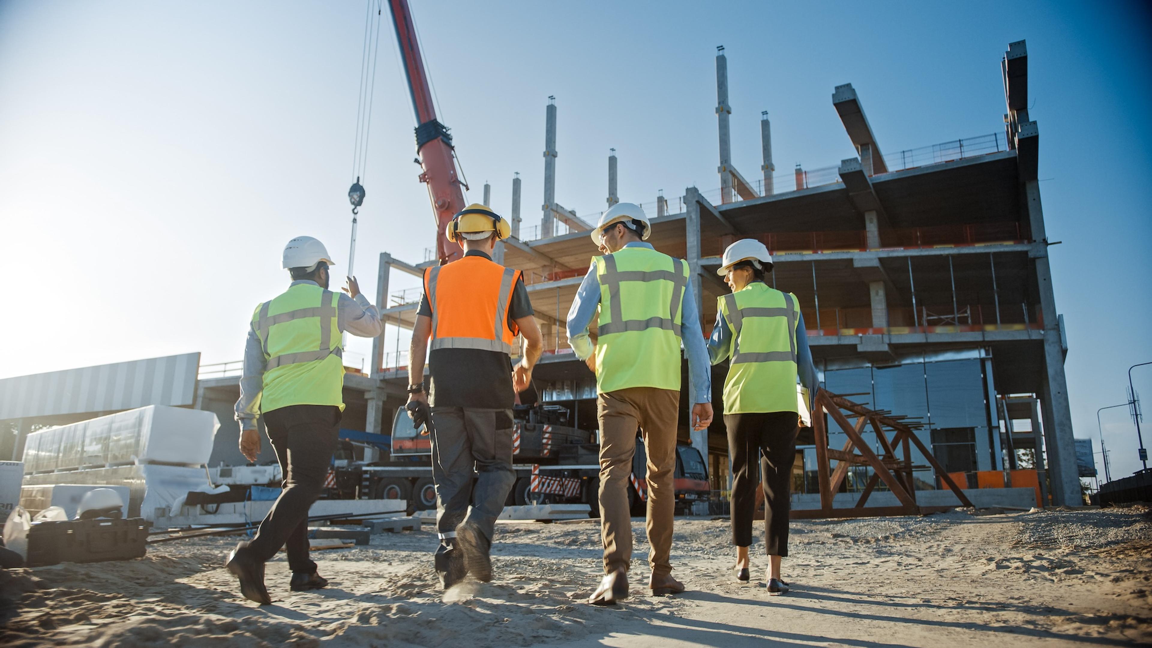 4 men in hi vis and hardhats walking onto a construction site