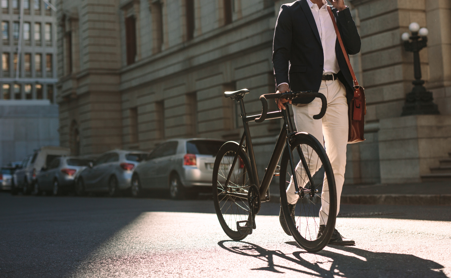 A businessman wheels his bicycle through a sunlit city street