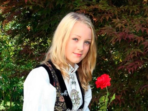 Portrait of person wearing a Norwegian traditional costum and holding a red rose.