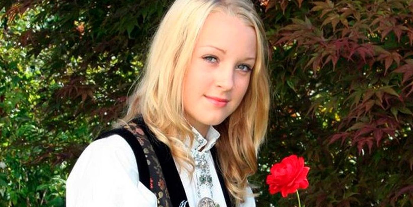 Portrait of a young woman in Norwegian national costume with a rose. Trees are seen in the background. Photo