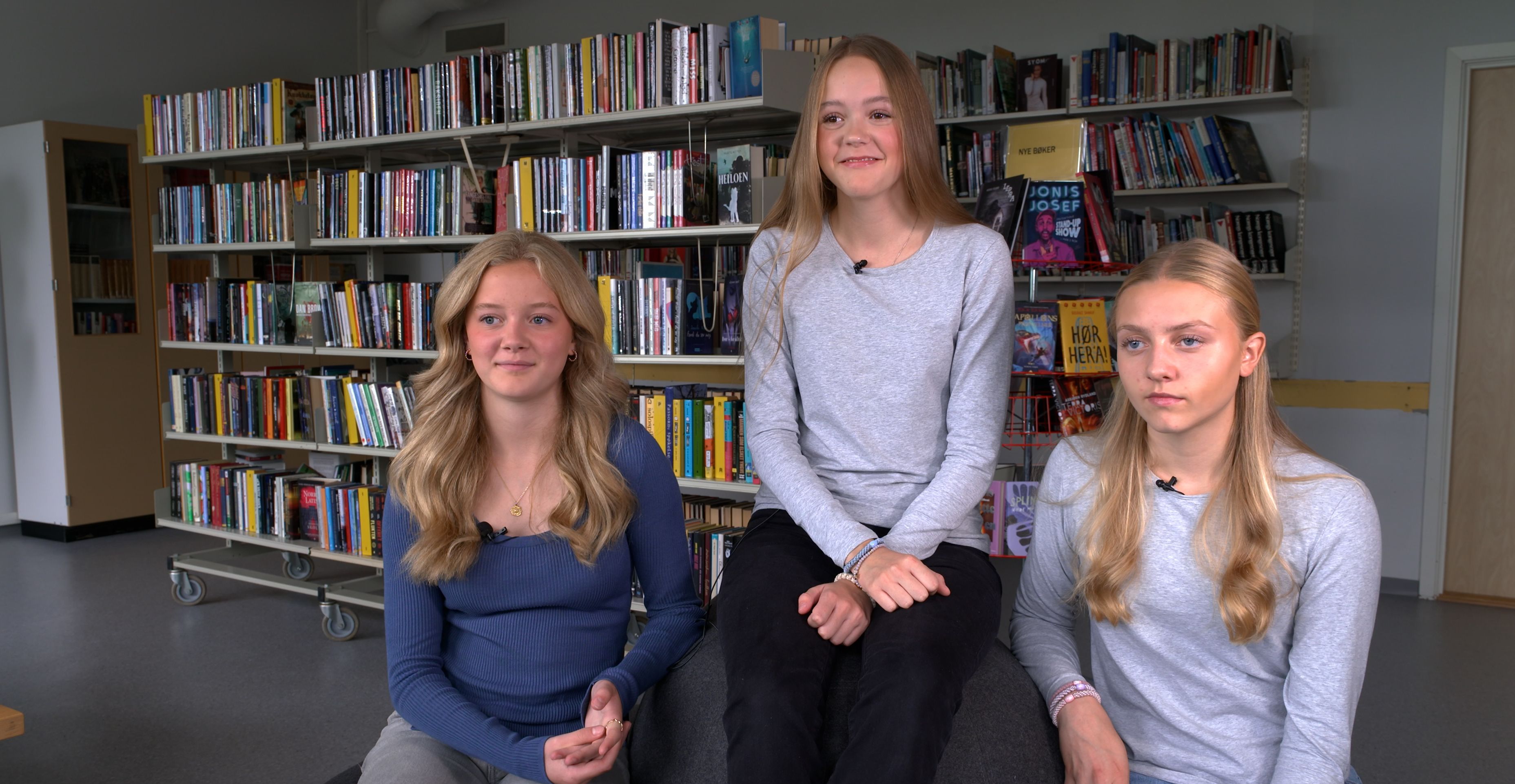 Tre jenter sitter i skolens bibliotek