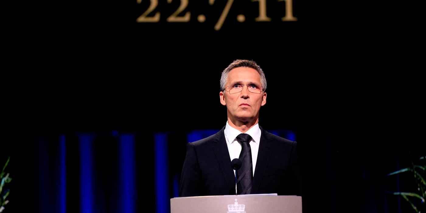 Suited man on lectern. In the background a wall with the inscription "22.7.11".