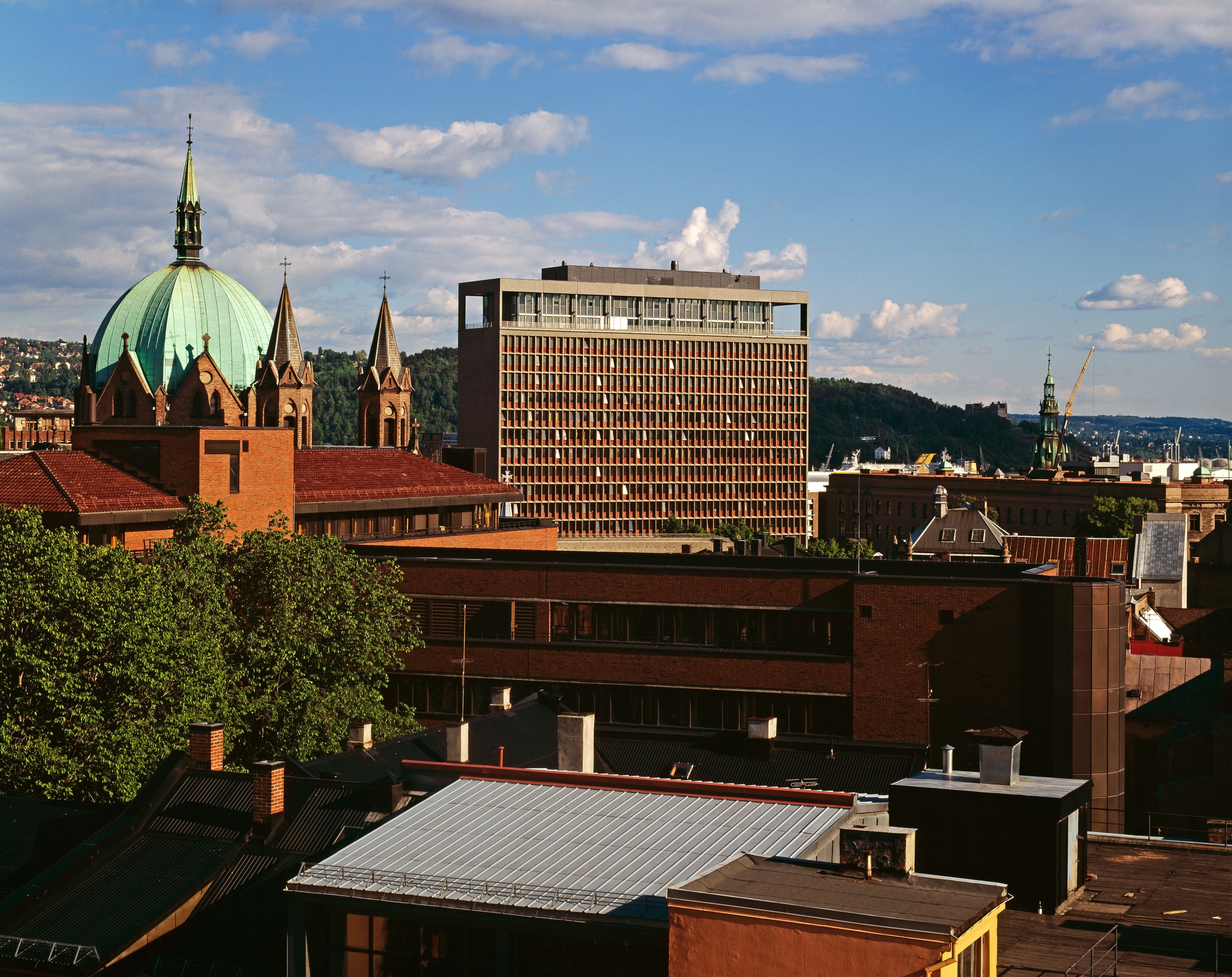 City in sunshine. A tall building and a church. Several small buildings.