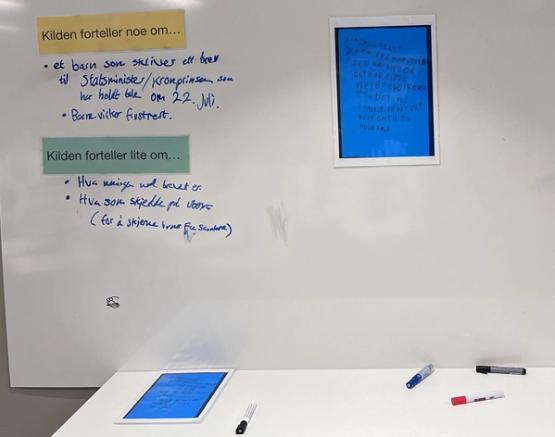 A white board with a large blue rectangle in the middle, a child's letter about July 22nd. To the left on the board, there are two headings stating 'the source tells something about...' and 'the source tells little about...'. Someone has filled in answers with a blue marker under each heading.