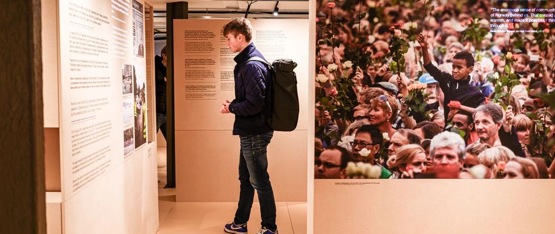 Exhibition elements showing the rose march with an unknown number of people lifting roses. Boy in front. A person stands reading exhibition text in the background.