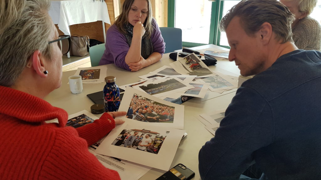 Tre personer sitter rundt et bord. Det ligger ulike bilder på bordet.
