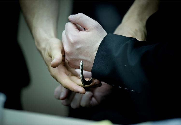 Three hands. Two hands in handcuffs. Man in suit. Blurred background