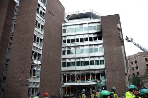 Foto av en skadet bygning med en helikopterplattform. Brannmenn og nødetatene er rundt bygningen. En brannbilstige til høyre for bygget.
