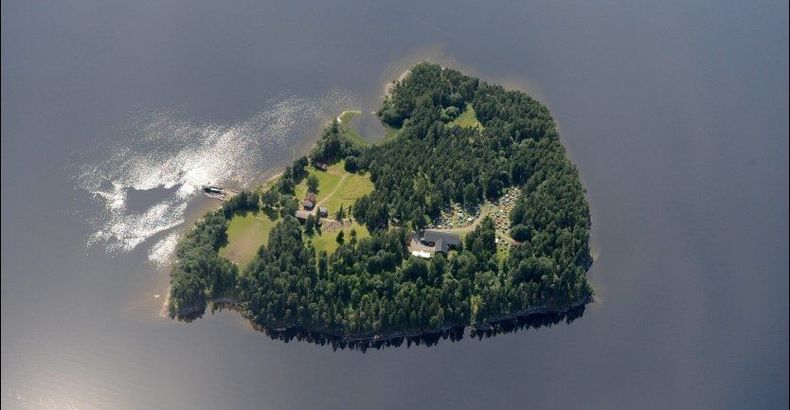 Flyfoto av øy i sol. Vann rundt.