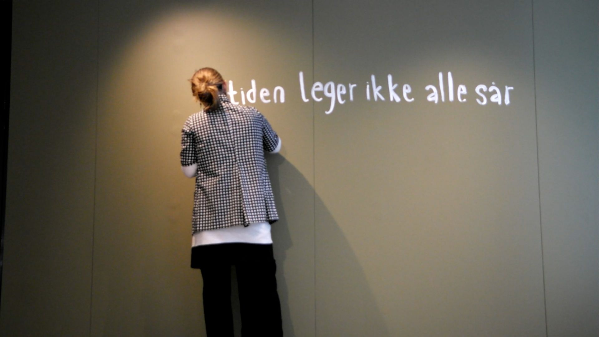 Woman, back against camera, writing with white paint on green wall.