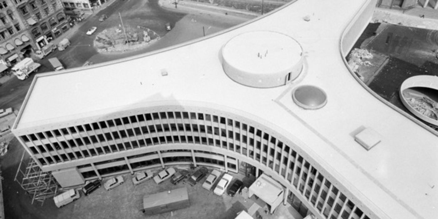 Aerial view in black and white of a Y-shaped modernist building. Some cars are parked next to the building.