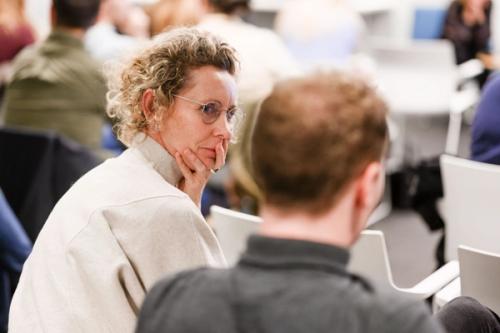 Close-up of a lady in a white sweater and light short hair and a man in a gray shirt. Blurred image, where you can see people in the background.