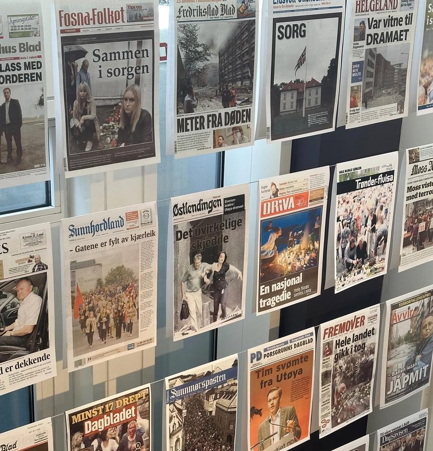 Many newspapers hang in a window. All have headlines about 22 July 2011.