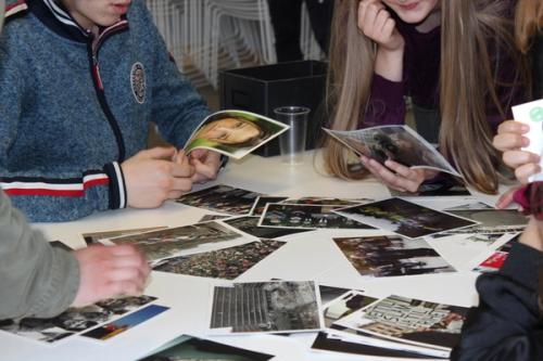 Four young people sit at a table and look at various pictures. In some of the pictures one can see buildings, faces, crowds.