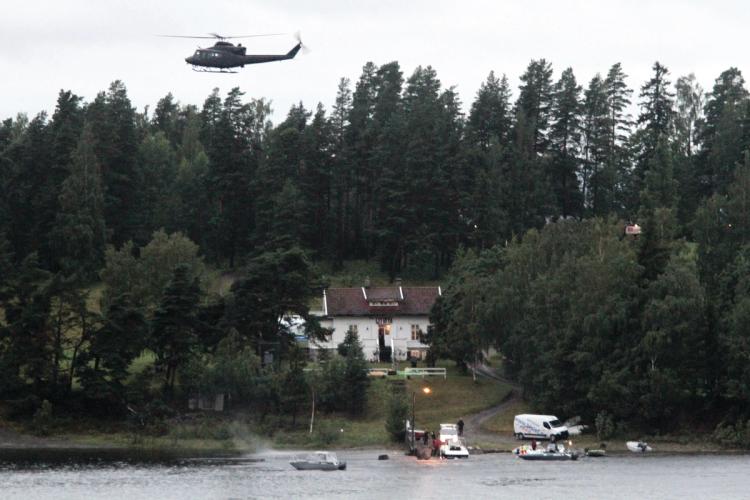 View towards the island. Boats at the dock. White house among trees. Helicopter in the air. Gray sky